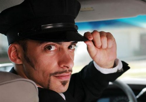 Portrait of a handsome male chauffeur sitting in a car saluting a viewer.